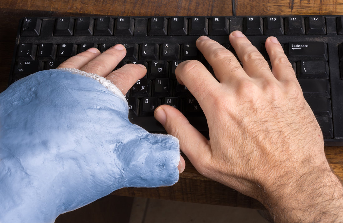 Picture of man's hands typin on keyboard left hand in a cast